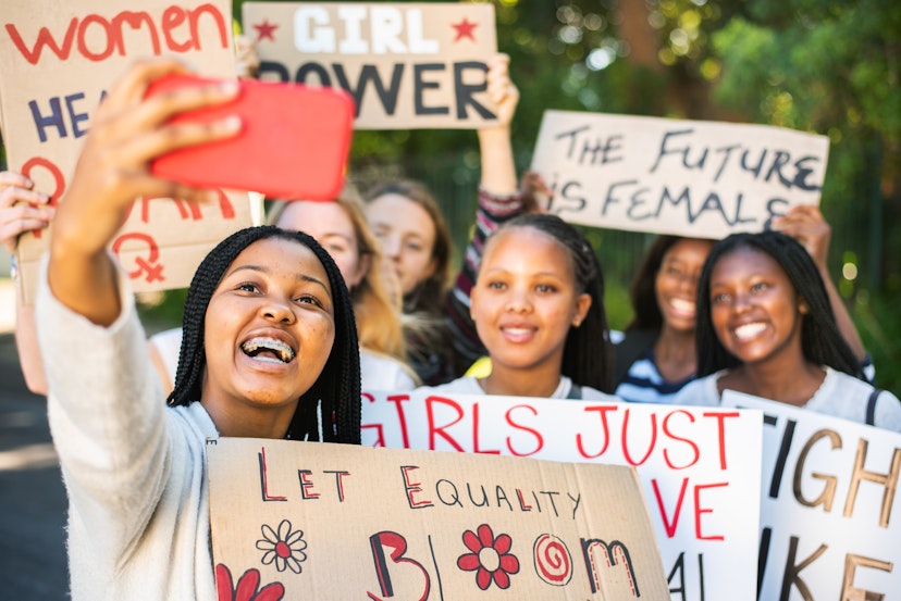 Diverse group of smiling teenage female friends with protest signs taking a selfie with a smart phone during a women's rights march